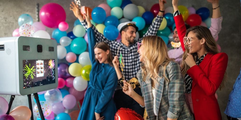 People in good mood taking photos in front of photo booth, having fun, using props and balloons.